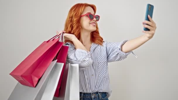 Fiatal vörös hajú nő, hogy szelfi okostelefon gazdaság bevásárló táskák felett elszigetelt fehér háttér - Felvétel, videó
