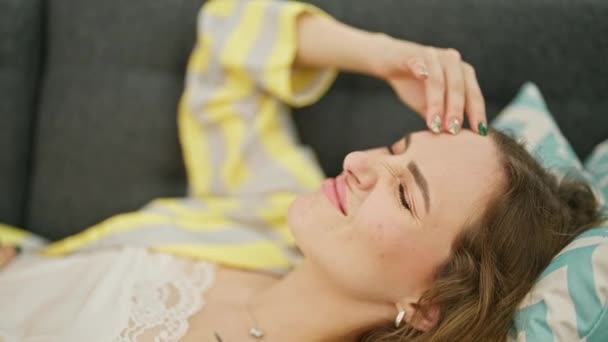 Νεαρή ξανθιά γυναίκα ξαπλωμένη στον καναπέ που υποφέρει από πονοκέφαλο στο σπίτι - Πλάνα, βίντεο