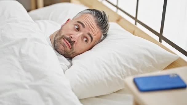 Hombre de pelo gris despertando para una llamada de teléfono inteligente en el dormitorio - Metraje, vídeo