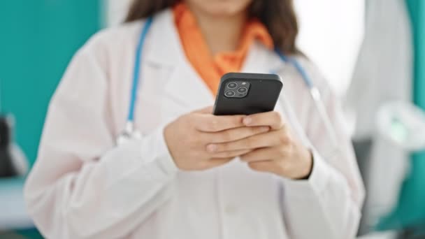 Young beautiful hispanic woman doctor using smartphone at clinic - Footage, Video
