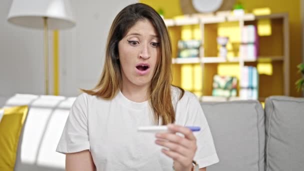 Jeune femme blonde tenant un test de grossesse avec expression inquiète à la maison - Séquence, vidéo