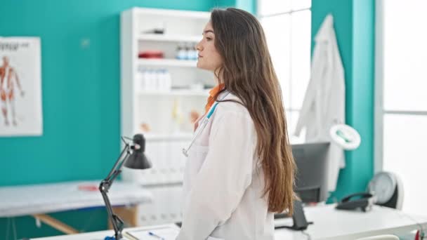 Νεαρή όμορφη Ισπανίδα γιατρός χαμογελά σίγουρος στέκεται με τα χέρια σταυρωμένα χειρονομία στην κλινική - Πλάνα, βίντεο