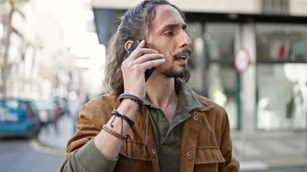 Молодой латиноамериканец разговаривает по смартфону с серьезным выражением на улице - Кадры, видео