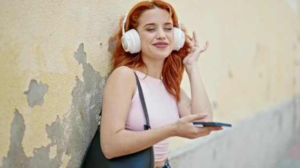 Fiatal vörös hajú nő zenét hallgat az utcán - Felvétel, videó