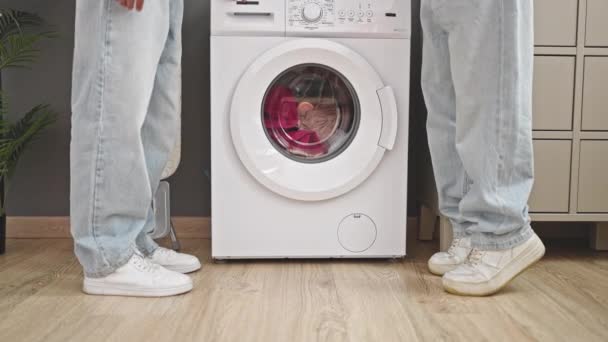 Dos hombres pareja esperando a la lavadora de pie en la sala de lavandería - Imágenes, Vídeo