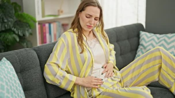 Jeune femme blonde souffrant de douleur menstruelle mettre sac d'eau chaude sur le ventre à la maison - Séquence, vidéo
