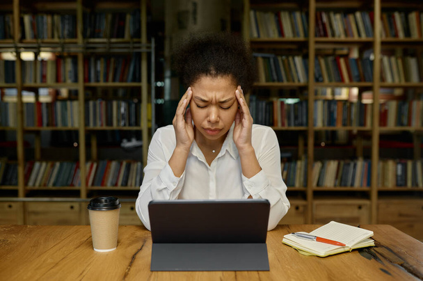Tired overworked female office worker touching head massaging temples suffering from headache or tension while sitting at desk table front of computer - Photo, Image
