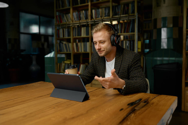 Liikemies, jolla on kuulokkeet ja videoneuvottelu työpöydän ääressä kannettavan tietokoneen kanssa. Online-kokous, digitaalinen viestintä, virtuaalinen chat-tiedotustilaisuus - Valokuva, kuva