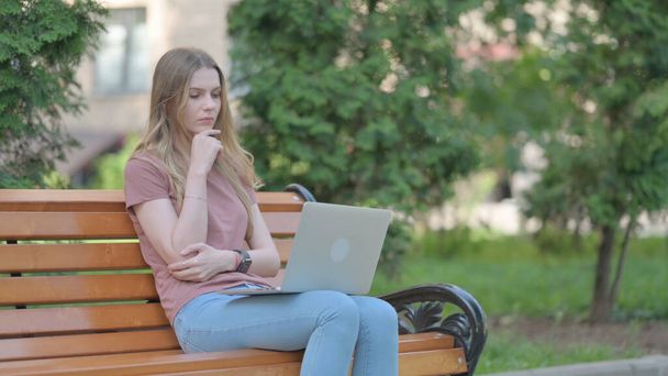 Junge Frau denkt und arbeitet draußen am Laptop - Foto, Bild