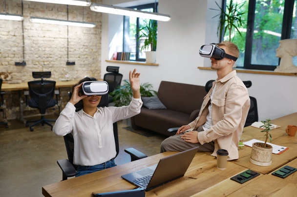 Inspired man and woman coworker wearing vr goggles in office. Male and female colleagues in virtual reality headset playing online games using cyberspace for business meeting and communication - Photo, Image