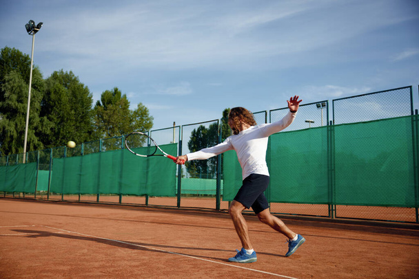 Профессиональный теннисист с ракеткой играет в игру на открытом поле. Спортивные занятия на свежем воздухе - Фото, изображение