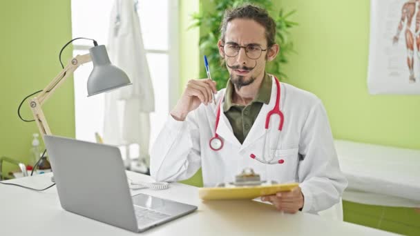 Νεαρός ισπανόφωνος γιατρός χρησιμοποιώντας το laptop γράφοντας στο πρόχειρο στην κλινική - Πλάνα, βίντεο