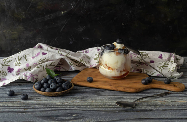 Het dessert. Heerlijk ijs in een glas met siroop en bosbessen op een houten tafel close-up - Foto, afbeelding