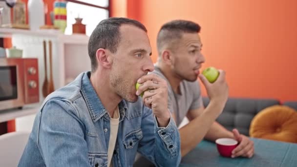 Dos hombres en pareja sentados en la mesa comiendo manzana en el comedor - Imágenes, Vídeo