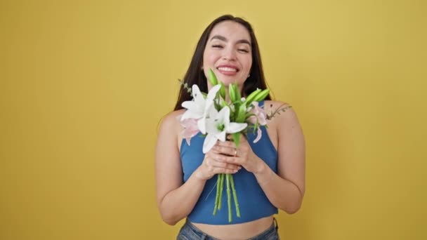 Giovane bella donna ispanica profumo bouquet di fiori sorridente su isolato sfondo giallo - Filmati, video