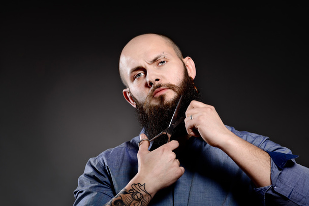  Ritratto di uomo che si taglia la barba con le forbici e guarda la macchina fotografica
 - Foto, immagini