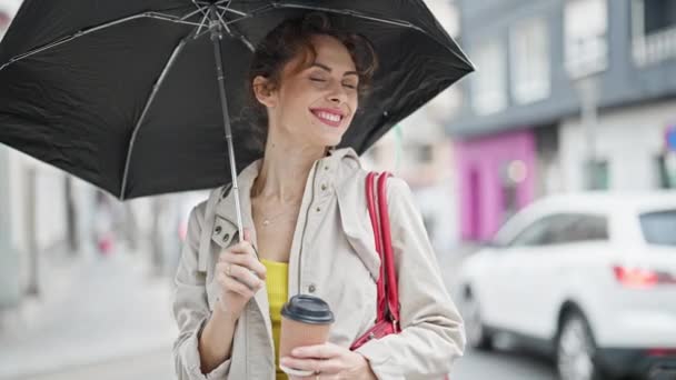 Fiatal nő kezében esernyő és kávé mosolyog az utcán - Felvétel, videó