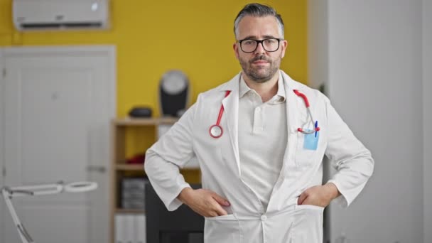 Doctor hombre de pelo gris sonriendo confiado de pie en la clínica - Imágenes, Vídeo