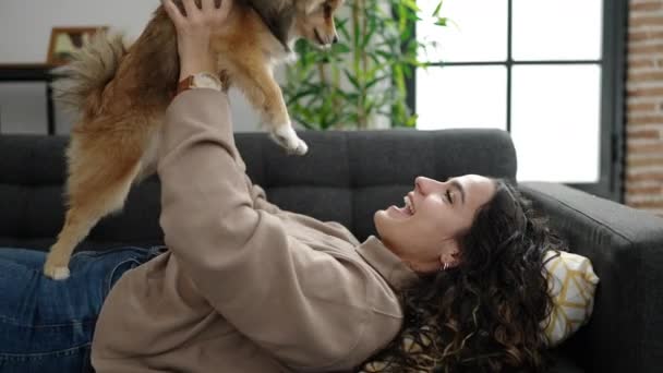 Mujer hispana joven con perro acostado en el sofá jugando en casa - Metraje, vídeo