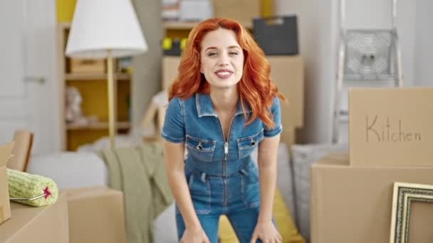 Jeune rousse femme souriante confiante assise sur le canapé avec les bras croisés geste à la nouvelle maison - Séquence, vidéo