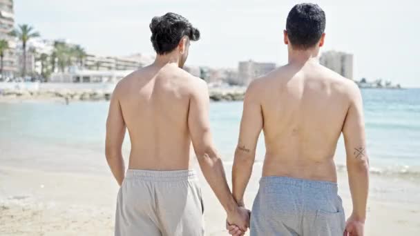 Két férfi turista pár kéz a kézben sétál a parton. - Felvétel, videó