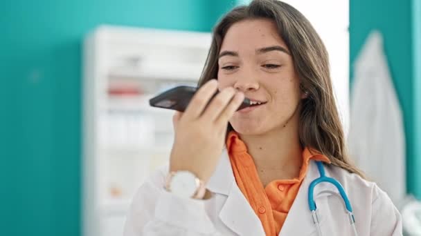 Joven hermosa mujer hispana médico enviando mensaje de voz sonriendo en la clínica - Imágenes, Vídeo