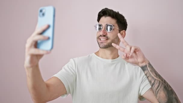 Jonge Spaanse man glimlachend zelfverzekerd selfie maken door de smartphone over geïsoleerde roze achtergrond - Video