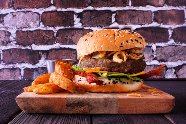 Delicious hamburger with cheese, bacon and crispy onions. Side view table scene against a dark brick background. - Photo, Image