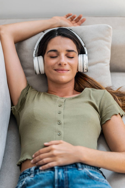 Shot of beautiful kind woman relaxing while listening music with headphones lying on couch at home - Photo, image