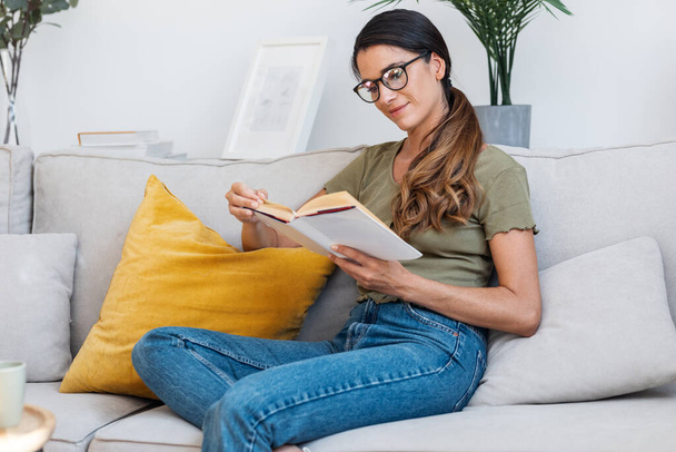 Shot of confident woman reading a book while sitting on sofa at home. - Foto, afbeelding