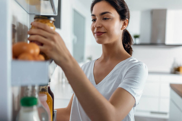 Shoot of beautiful young woman taking some healthy food from the fridge in the kitchen at home - Fotoğraf, Görsel