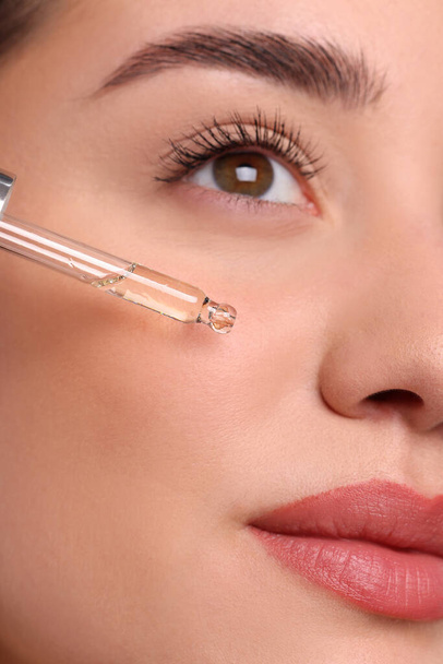 Young woman applying essential oil onto face, closeup - Zdjęcie, obraz