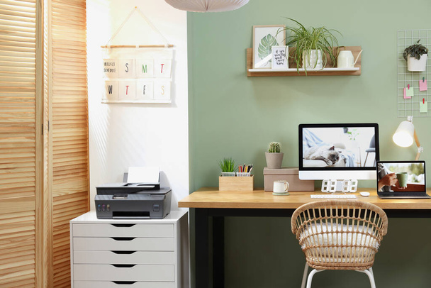 Stylish workplace with computer, laptop and lamp near olive wall at home - 写真・画像