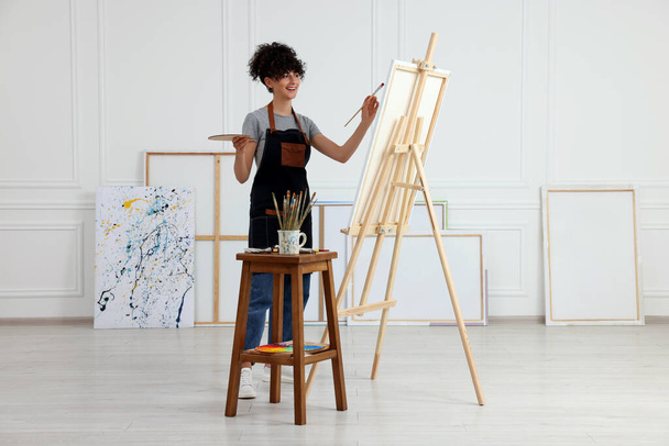 Young woman painting on easel with canvas in studio - Foto, immagini