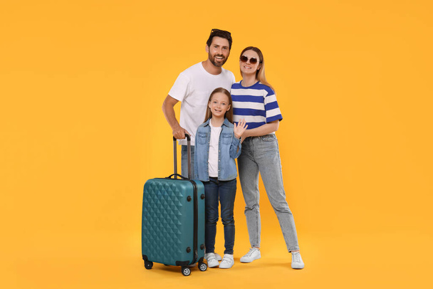 Happy family with green suitcase on orange background - Foto, imagen