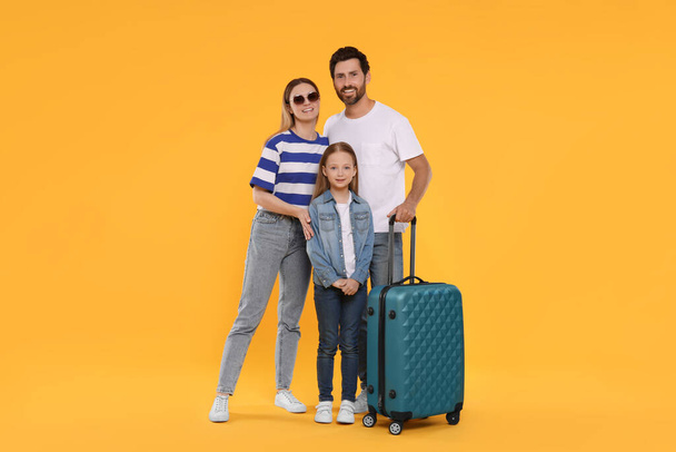 Happy family with green suitcase on orange background - Фото, зображення