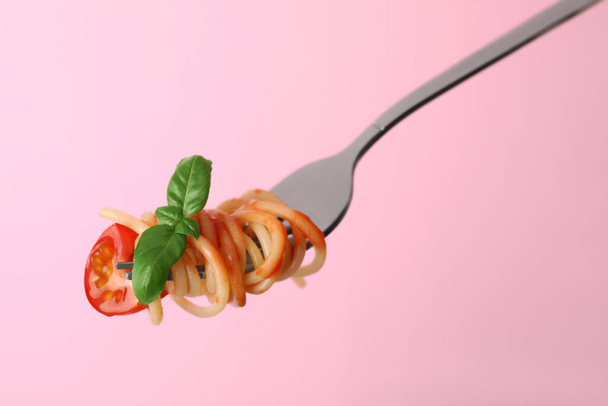 Tasty pasta with tomato sauce and basil on fork against pink background, closeup - Foto, imagen