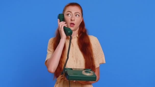 Jonge volwassen moe slaperige vrouw praten op bedraad vintage telefoon van de jaren 80 met een vriend, het maken van een gesprek. ongeïnteresseerd roodharige meisje hebben geërgerd saai praten geïsoleerd op blauwe studio achtergrond - Video