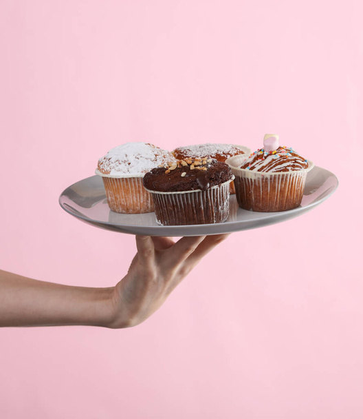 Женская рука держит тарелку кексов на розовом фоне - Фото, изображение