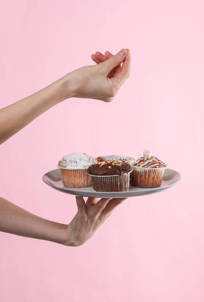vrouwenhand met een bord cupcakes op een roze achtergrond - Foto, afbeelding