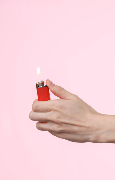 Encendedor llameante en una mano femenina sobre un fondo rosa - Foto, imagen