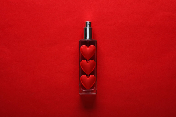 Frasco de perfume con corazones sobre fondo rojo. Concepto de belleza, día de San Valentín - Foto, Imagen
