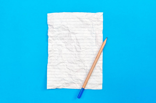 Crumpled notepad sheet with pencil on blue. - Fotografie, Obrázek