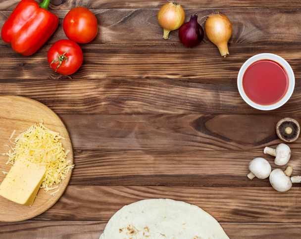 Ingrediënten voor het koken van pizza op tafel. Tomaten, zoete rode peper, champignons, ui, geraspte kaas en deeg. Bovenaanzicht. Kopieerruimte. - Foto, afbeelding
