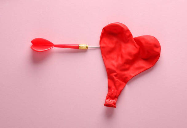 Dardo e infla globo en forma de corazón rojo sobre fondo rosa. Concepto de amor - Foto, Imagen
