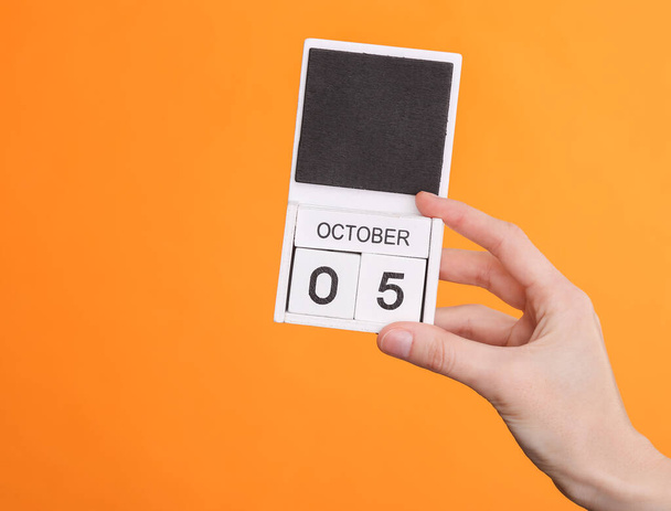 Drewniany kalendarz blokowy z datą 05 października w ręku kobiety na pomarańczowym tle - Zdjęcie, obraz