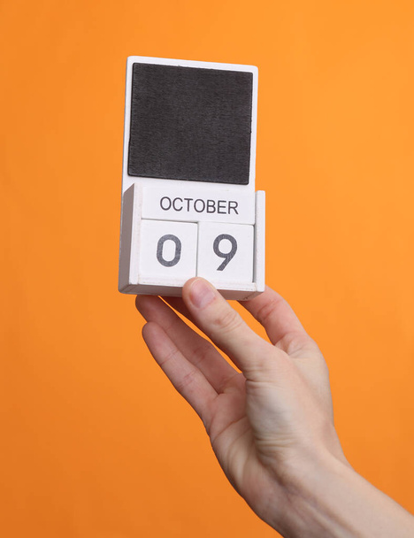 Holzblock-Kalender mit Datum Oktober 09 in weiblicher Hand auf orangefarbenem Hintergrund - Foto, Bild