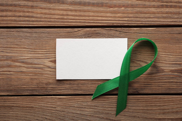Green awareness ribbon with white banner on wooden table - Photo, Image