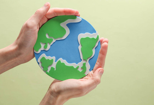 Female hands hold planet earth on green background. Save the planet - Фото, изображение