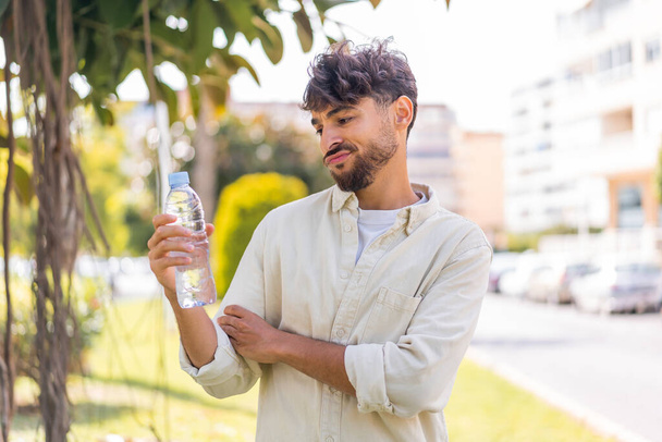Young Arabian handsome man with a bottle of water at outdoors with sad expression - Фото, зображення